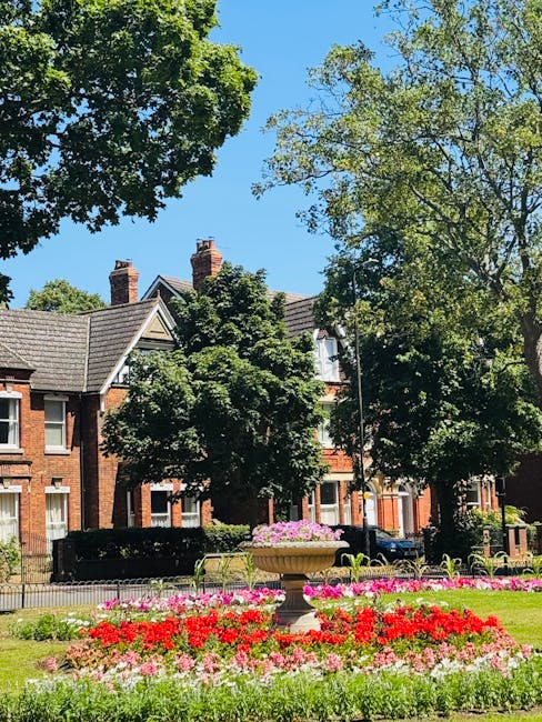 A charming front garden in front of a house with a vibrant blue door, featuring a lush green shrub on the left side and a variety of potted plants with red and orange flowers placed near the entrance.